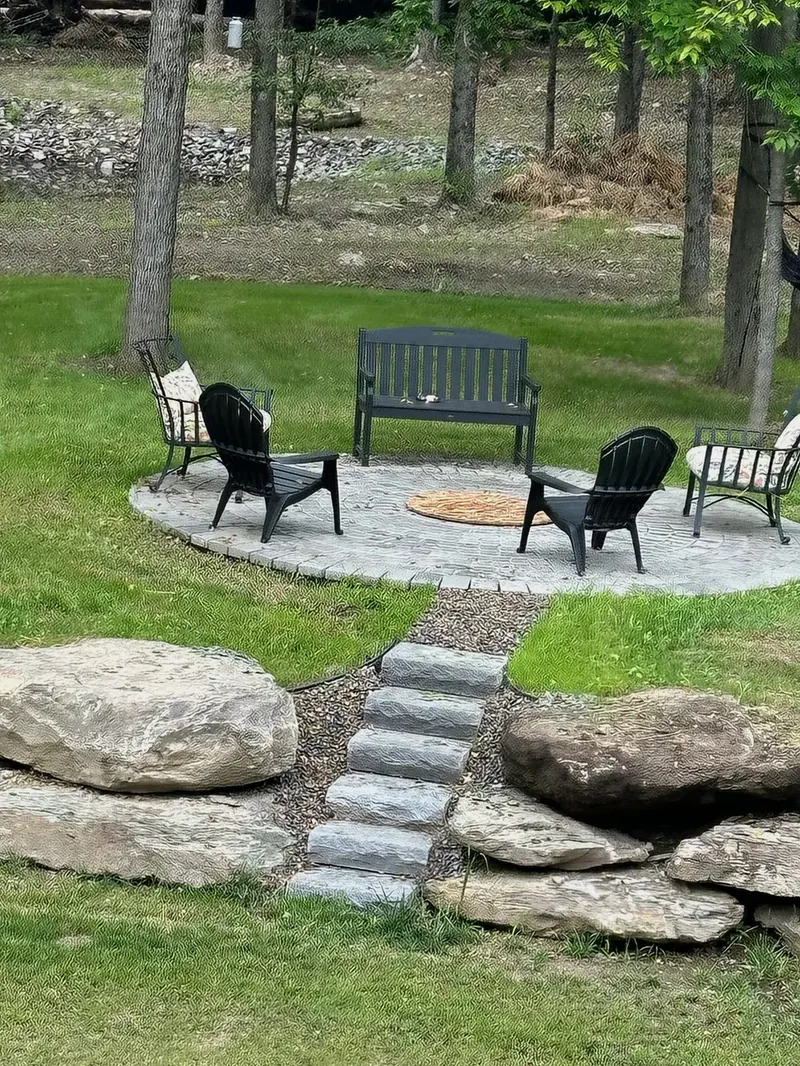 Sunken fire pit seating area ringed by natural boulders and stone steps in a wooded yard